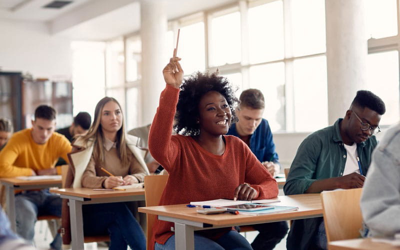 Black woman raises hand to answer question in class