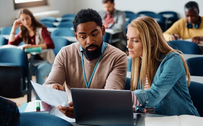 Black man and light-skinned blonde woman look over papers and computer