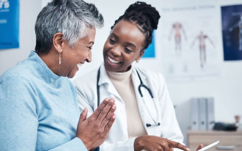 Elderly dark skinned woman happily conversing with her black female doctor
